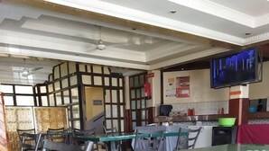 A restaurant with multiple tables and chairs, a kitchen area, and a television mounted on the wall.