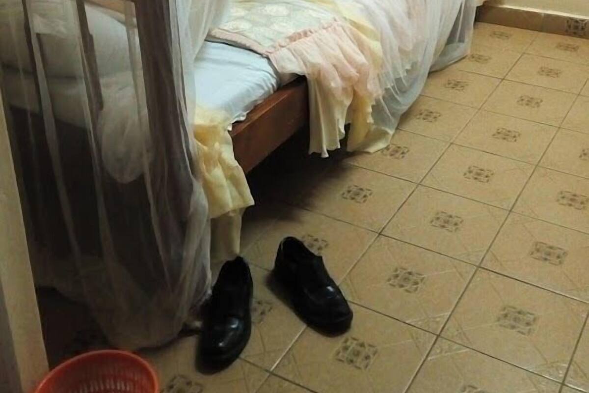Un lit simple avec un baldaquin, un panier rouge et une paire de chaussures noires sur un sol carrelé.