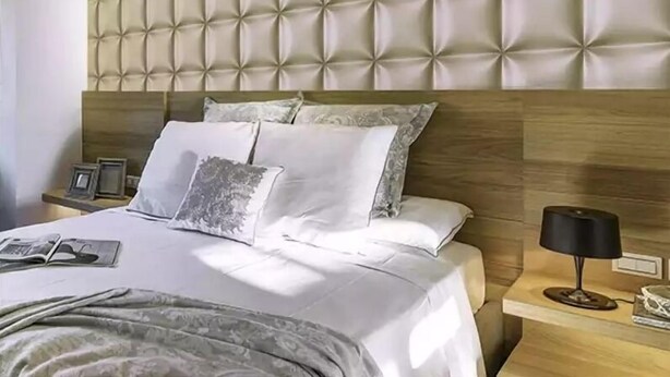 A modern bedroom with a tufted headboard, a neatly made bed with white linens, and a bedside table with a lamp and a framed picture.
