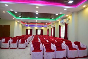 Un salón de conferencias con filas de sillas tapizadas en rojo y blanco, luces de techo y unidades de aire acondicionado.