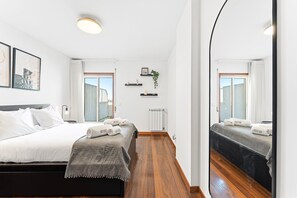 Una habitación de hotel moderna con una cama grande, un espejo, un radiador y una ventana con cortinas.