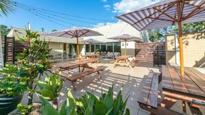 An outdoor patio area with wooden picnic tables and striped umbrellas, surrounded by potted plants and a brick wall. - Tahmoor Inn (Tahmoor)