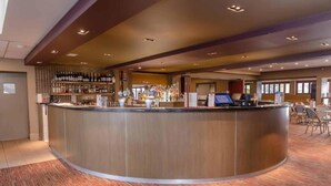 A modern hotel lobby with a curved reception desk, a bar area with a variety of liquor bottles, and a seating area with patterned chairs. - Tahmoor Inn (Tahmoor)