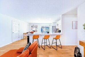 Eine moderne Küche mit Kochinsel, Barhocker und Essbereich mit einer Couch und Kissen.