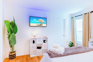 Ein Schlafzimmer mit Bett, Fernseher, Pflanze, Regal und Tür.