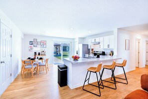 Eine moderne Küche mit einer zentralen Kochinsel, Barhocker, Holzstühlen und einem Esstisch.