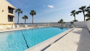 Une piscine rectangulaire à l’eau d’un bleu cristallin, entourée de chaises longues blanches et de palmiers.