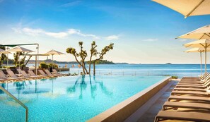 Zona de piscina con sillas de descanso y sombrillas, con vistas al mar tranquilo y una isla distante.