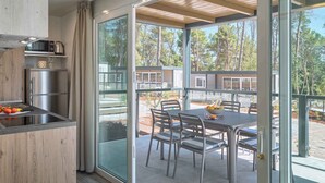 Una cucina moderna con forno e microonde integrati, un'area pranzo con tavolo e sedie, e una porta vetrata che dà su un terrazzo con vista sugli alberi.