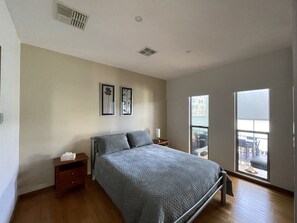 A bedroom with a bed, a nightstand, a window, and a view of the outdoors.
