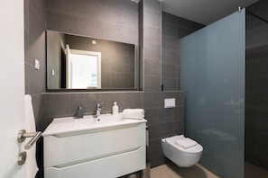 Un baño moderno con tocador blanco, un espejo grande y una cabina de ducha de vidrio.