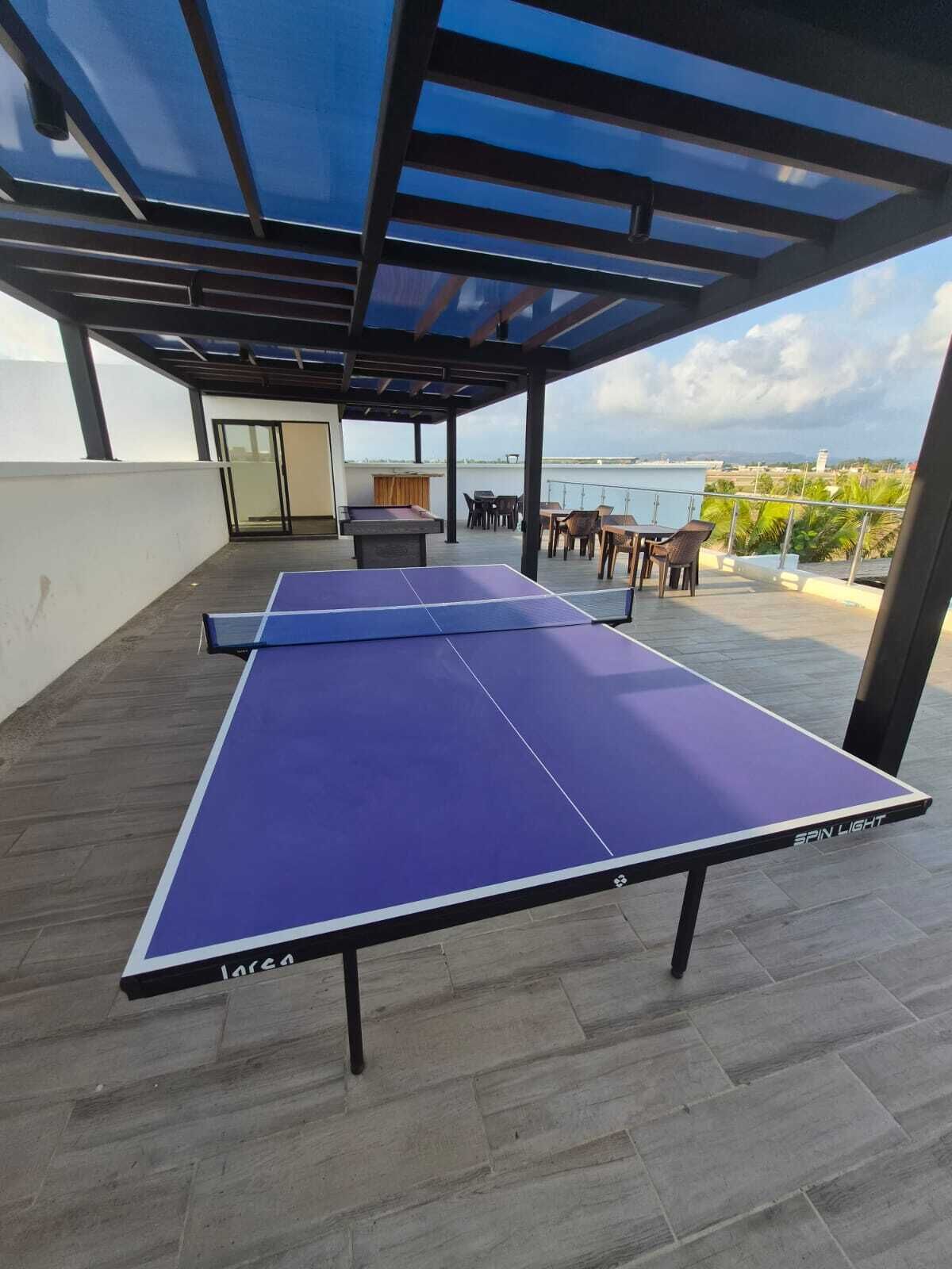 Una mesa de ping pong bajo un área techada con vista al mar.
