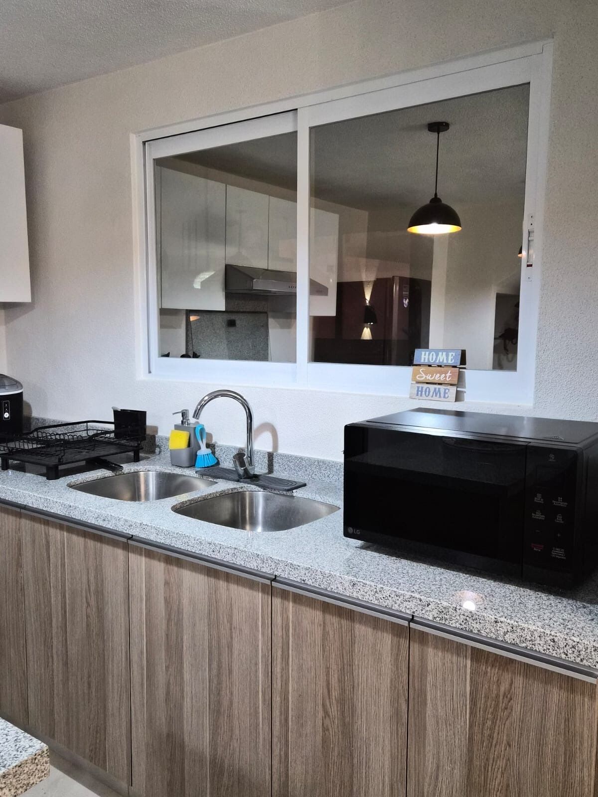 Een moderne keuken met granieten werkbladen, roestvrijstalen spoelbakken en een zwarte magnetron.