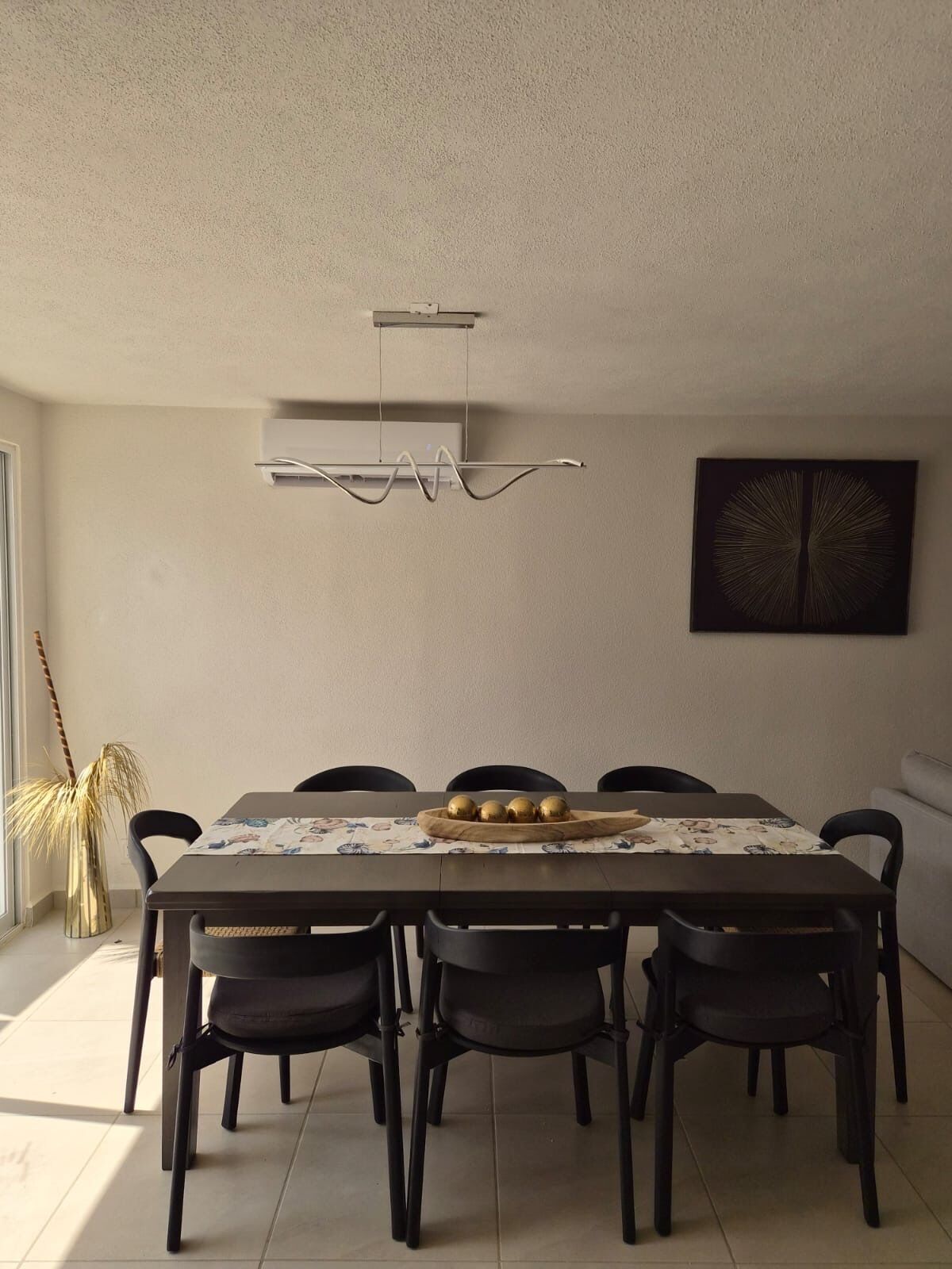 Un coin repas avec une table dressée pour six personnes, un luminaire suspendu moderne et un climatiseur fixé au mur.