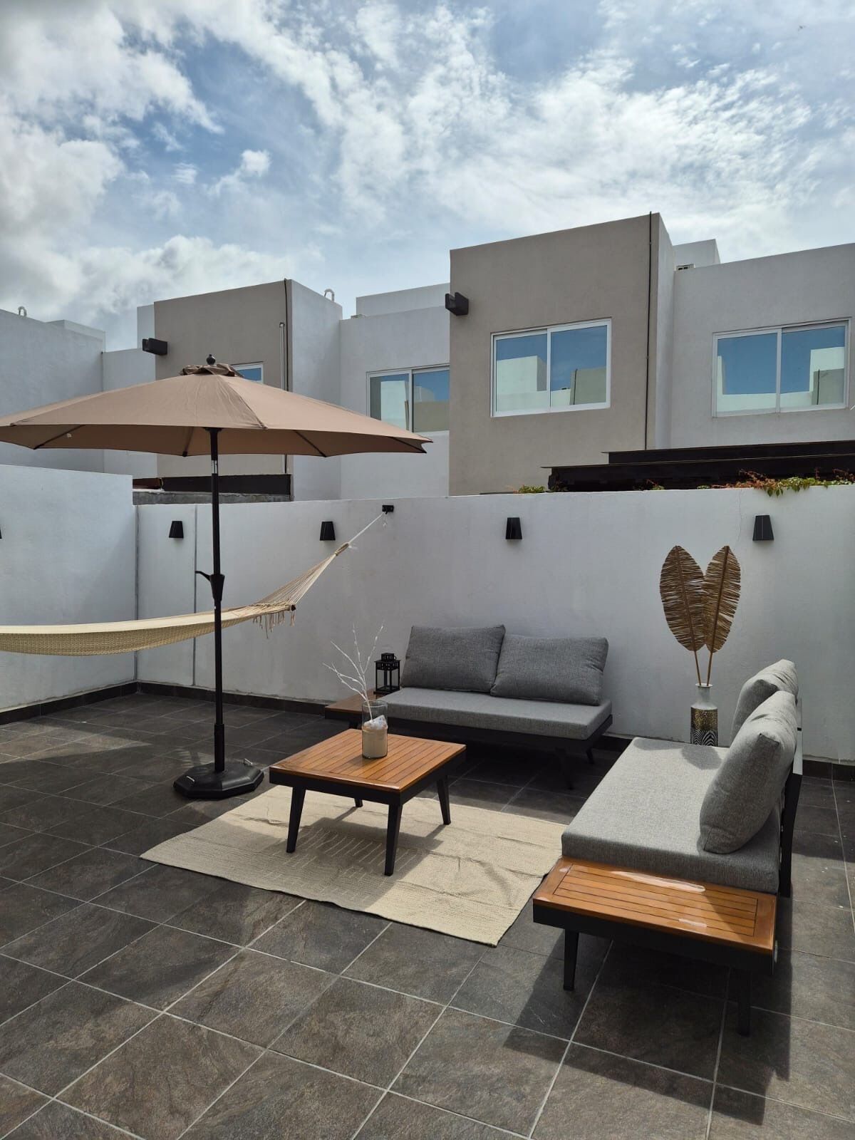 Un patio extérieur moderne, aménagé avec un hamac, un canapé, une table basse et un parasol.