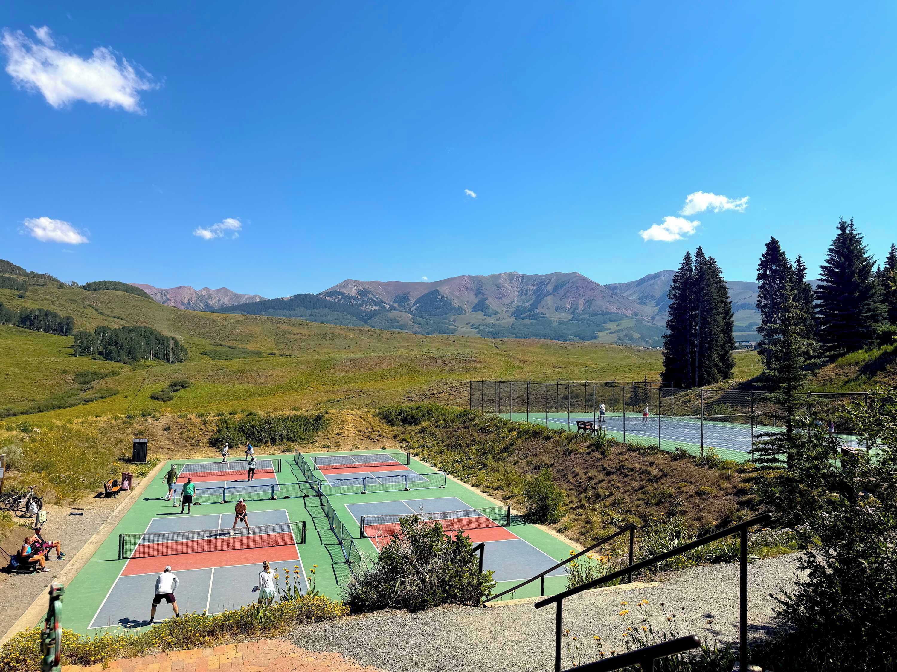 A tennis court with multiple courts, surrounded by a mountainous landscape.