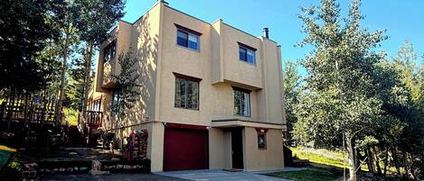 A two-story building with a red garage door, surrounded by trees and a gravel driveway.
