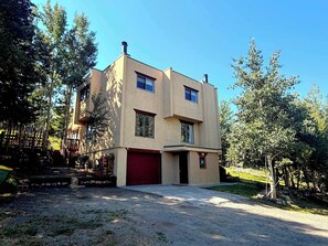 A two-story building with a red garage door, surrounded by trees and a gravel driveway. - Vintage Ski Haus Near Mt CB Wedding Garden (Crested Butte)