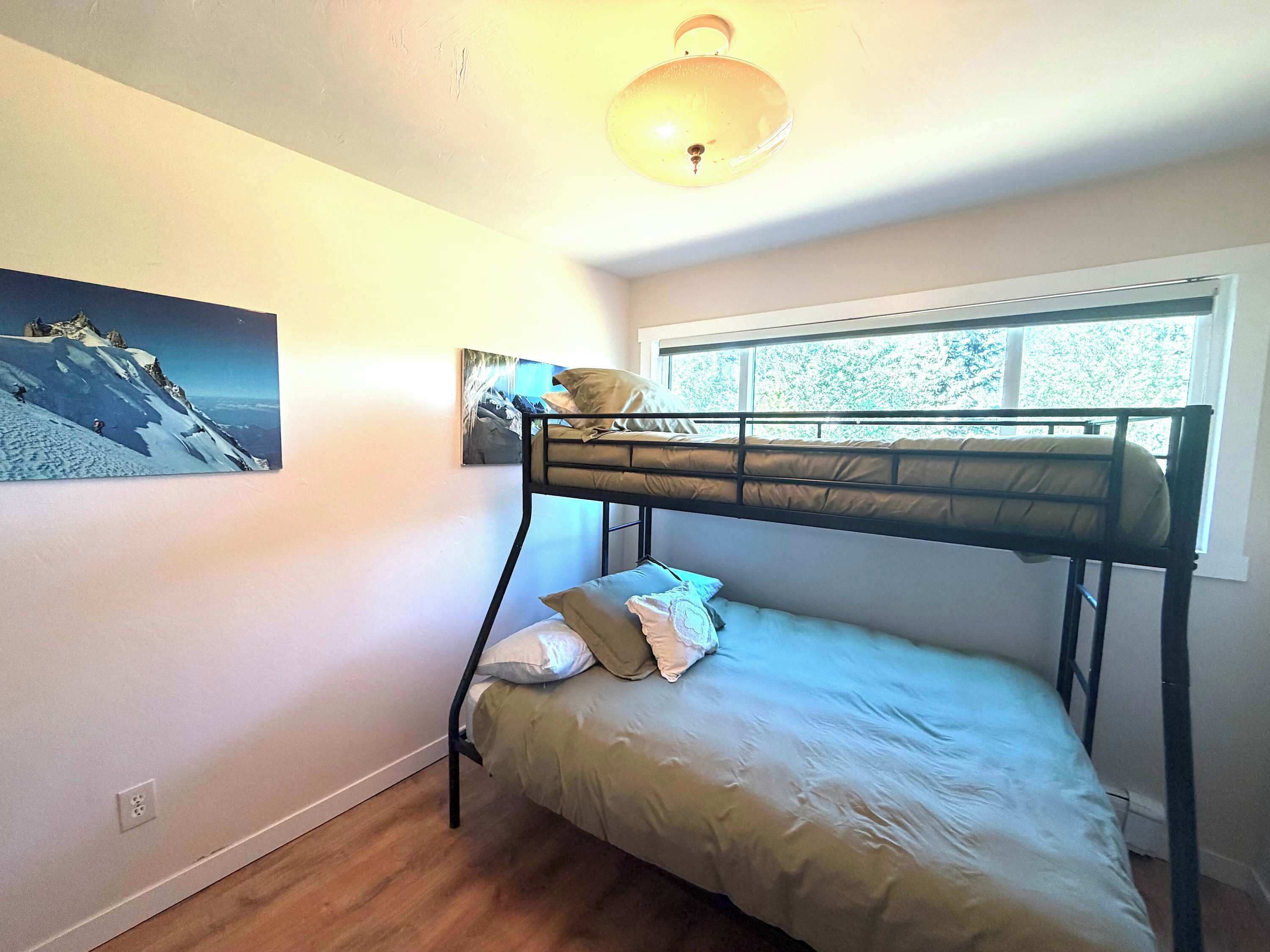 A bunk bed room with a window, a painting on the wall, and a ceiling light fixture.