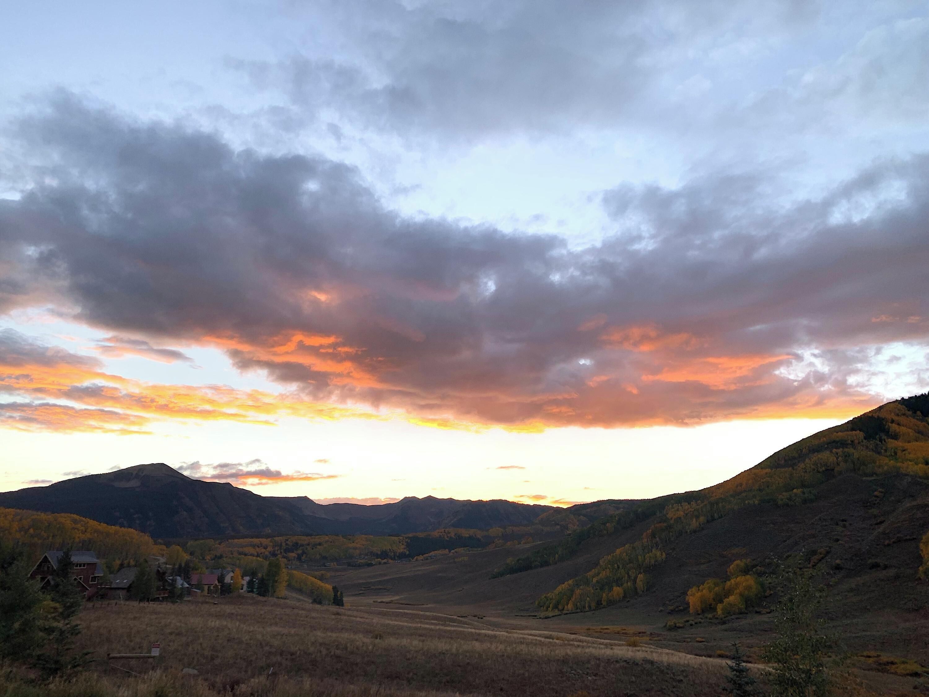 Un valle con una montaña al fondo y un cielo al atardecer.