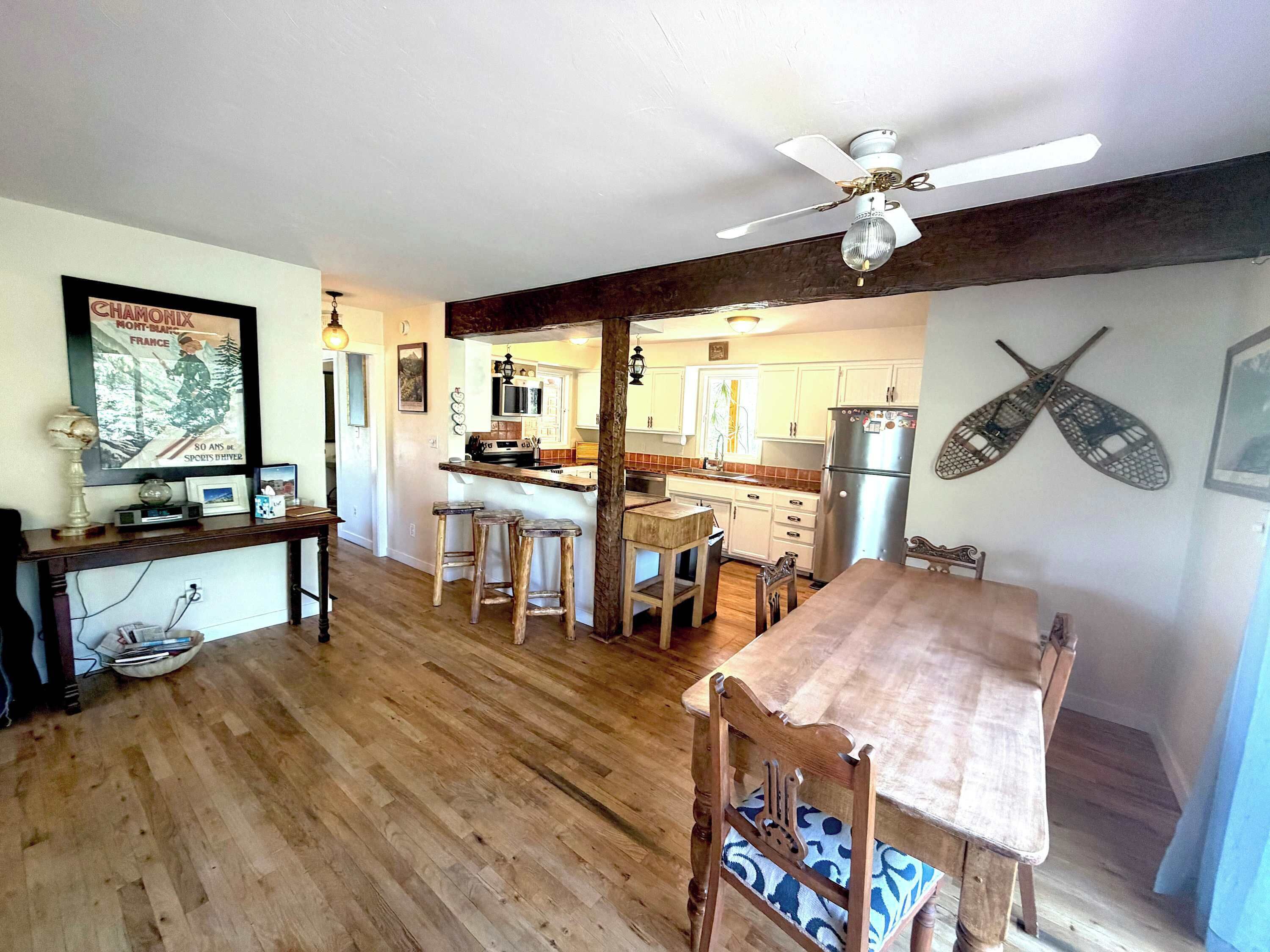 A kitchen with wooden flooring, a dining table with chairs, a ceiling fan, and a refrigerator.