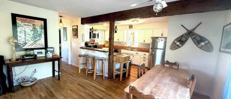 A kitchen with wooden flooring, a dining table with chairs, a ceiling fan, and a refrigerator.