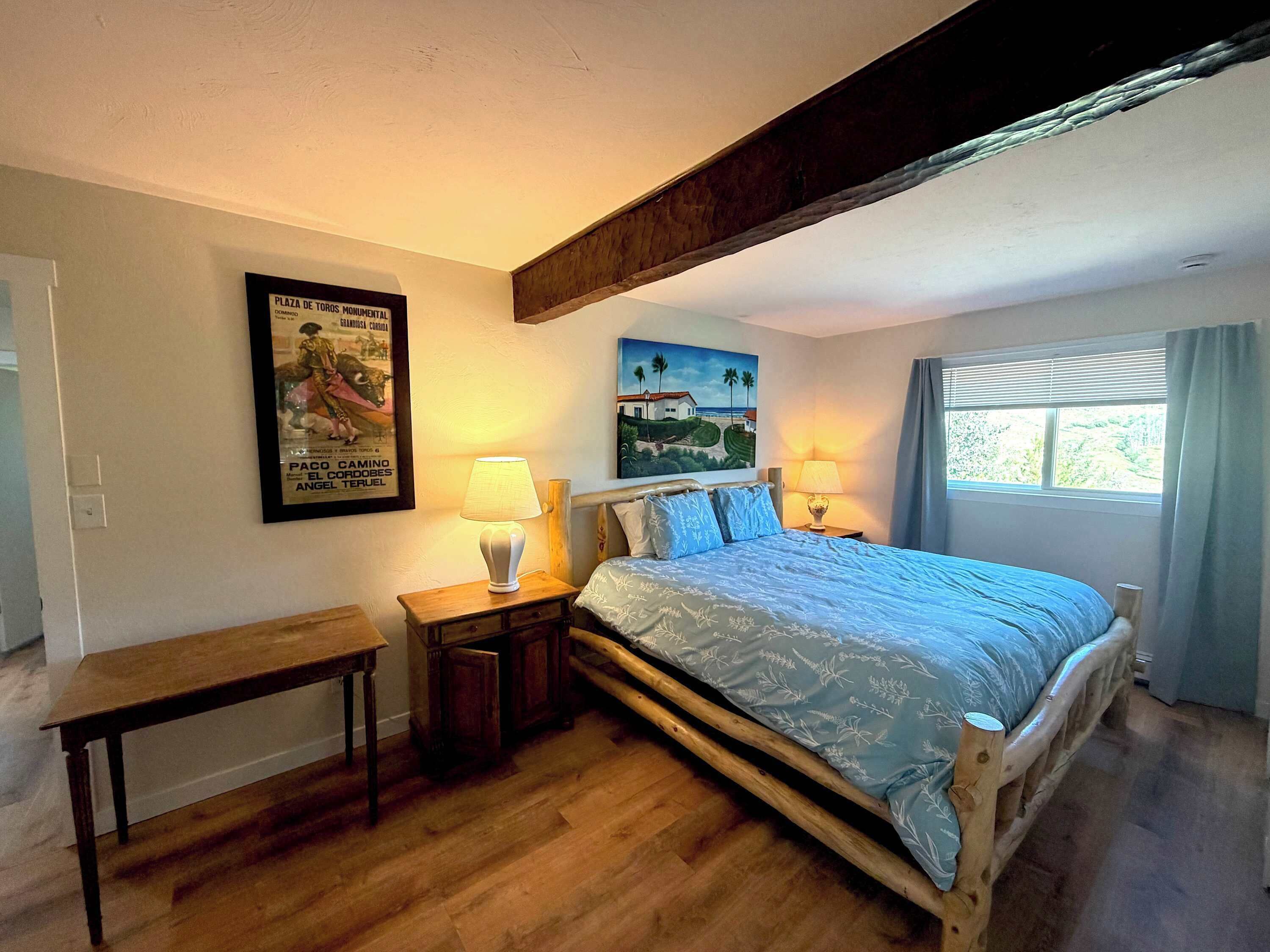 A bedroom with a wooden bed, two bedside tables with lamps, a bench, and artwork on the walls.