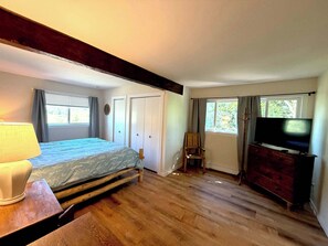 Ein Schlafzimmer mit einem Bett, einer Kommode, einem Fernseher und einem Fenster mit Vorhängen.