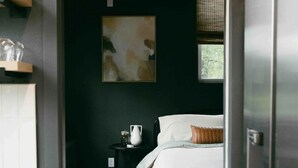 A narrow hallway leading to a bedroom with a bed, a nightstand, a small table, and a window with a view.