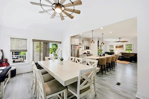 Una cocina amplia con electrodomésticos modernos, un comedor con mobiliario blanco y un ventilador de techo.