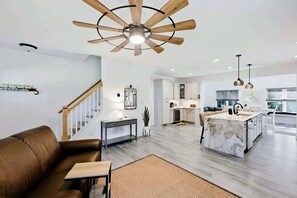 Una cocina moderna con una isla central, un rincón de comedor con un sofá de cuero marrón y una escalera con barandilla de madera.