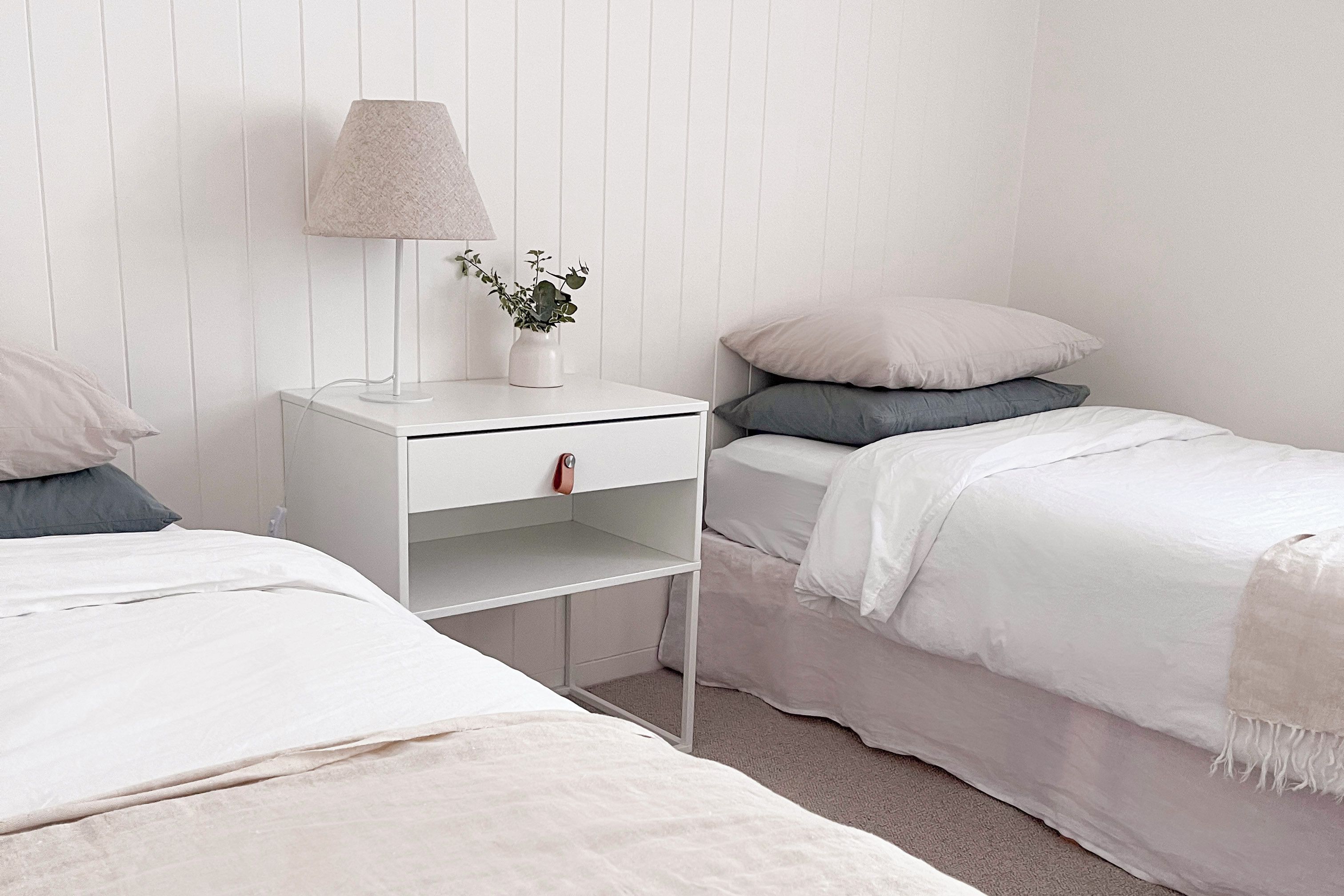 Une chambre avec deux lits, une table de chevet avec une lampe, une petite plante et une armoire blanche.