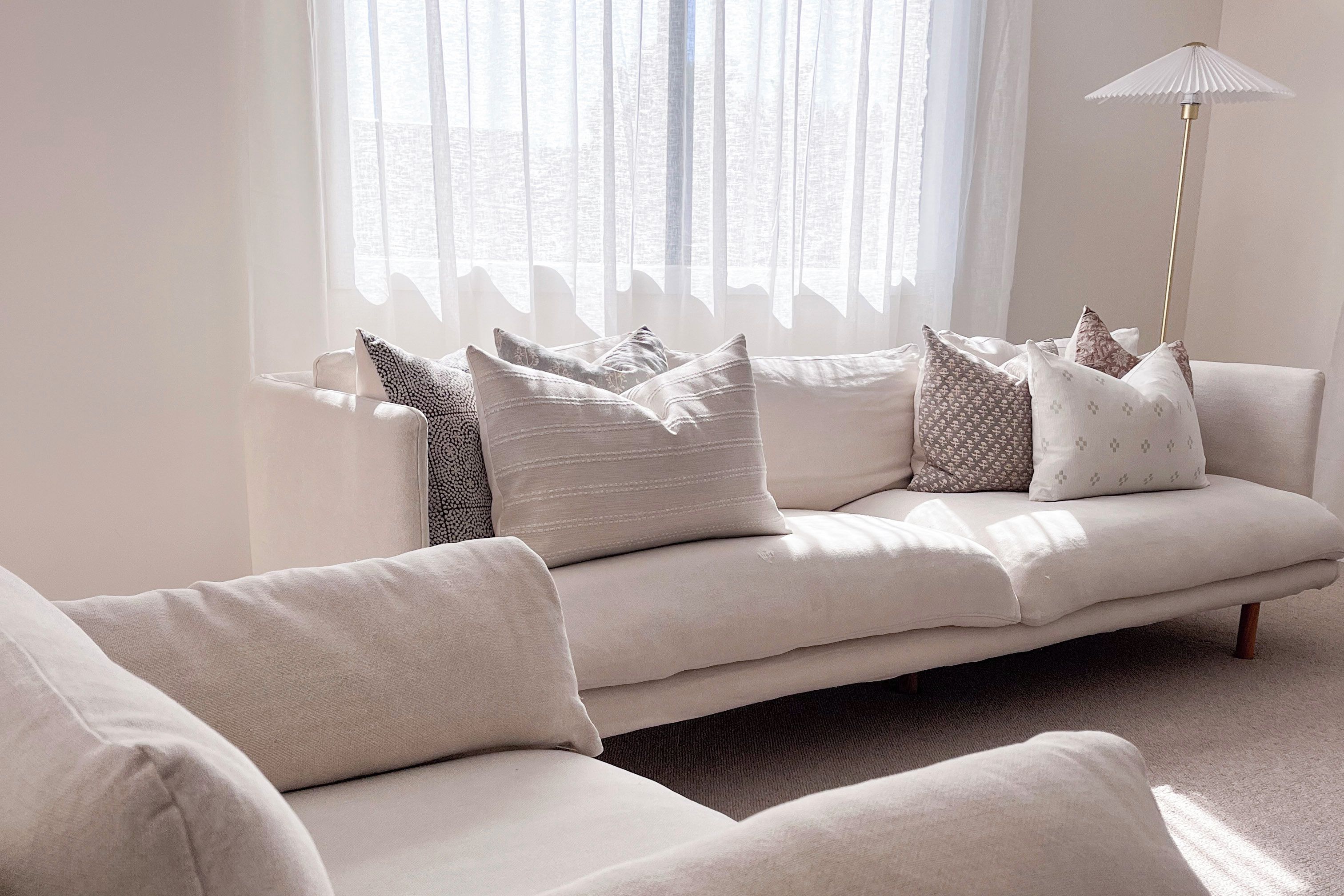 A modern living room with a beige sofa, patterned cushions, and a floor lamp.