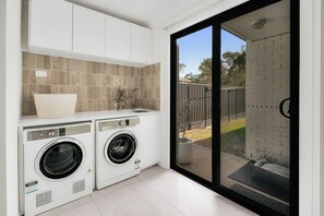 A laundry room with two front-loading washing machines, a sink, and a window overlooking a backyard. - Summers Green View Retreat - Kayaks Included (Logan Reserve)