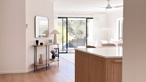 Une chambre d’hôtel moderne avec un plancher en bois, un comptoir de réception blanc, un grand miroir et une porte-fenêtre coulissante donnant sur un balcon.