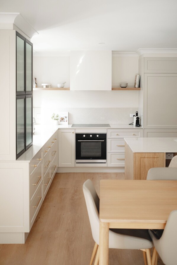 Une cuisine moderne avec des meubles blancs, un four encastré et un coin repas comprenant une table et des chaises en bois.