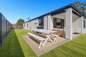 A modern outdoor patio area with a picnic table and seating, surrounded by a well-maintained lawn and a brick wall.