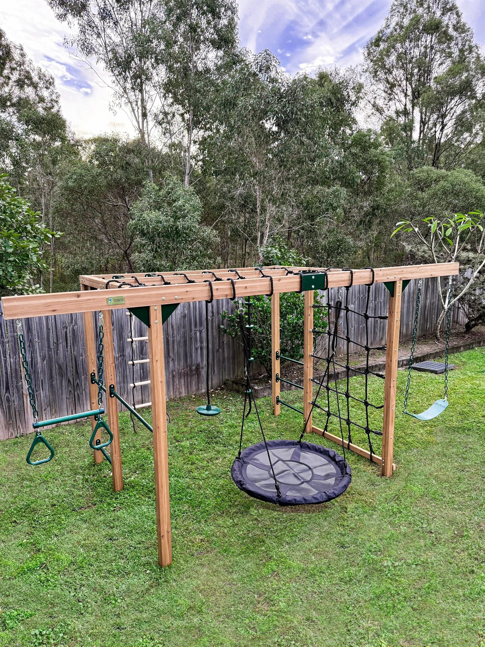 A wooden swing set with a trampoline and a slide in a backyard.