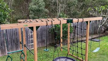 A wooden swing set with a trampoline and a slide in a backyard.