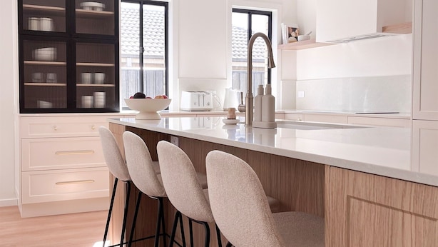 Une cuisine moderne dotée d’un îlot central, de tabourets de bar et d’un meuble encastré avec des portes en verre.