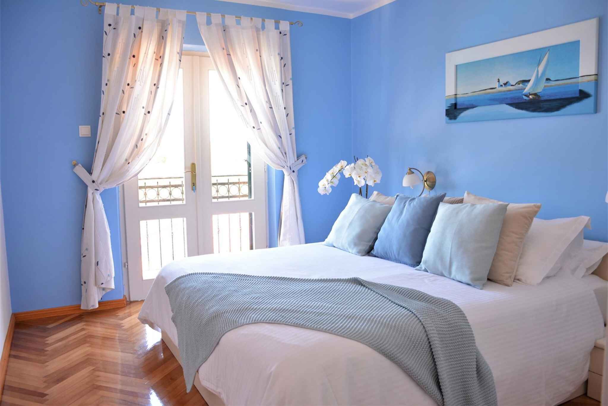 Un dormitorio con cama, cortinas, un cuadro y una ventana.