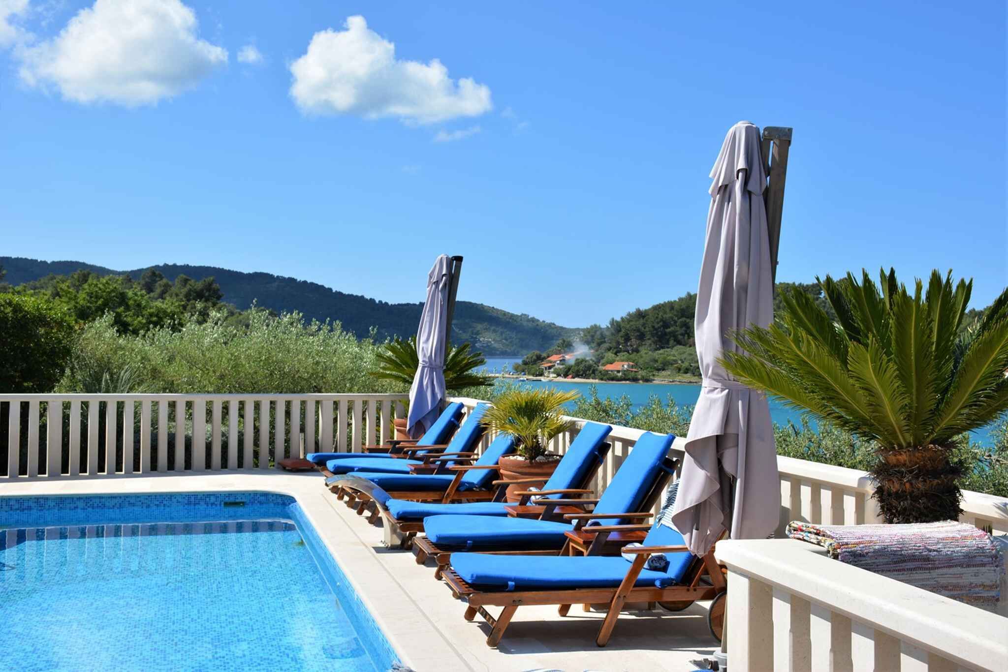 A poolside area with lounge chairs and umbrellas, overlooking a body of water and hills.