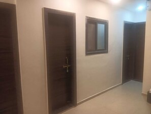 A hallway with three doors, one with a window, and a light fixture above. - Hotel Kulswamini Inn (Trimbak)