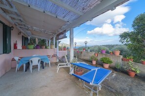 A covered outdoor patio with a table and chairs, surrounded by potted plants. - APPARTAMENTI LENTISCO - BILOCALE LENTISCO (Capoliveri)