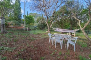 An outdoor seating area with a table and chairs, surrounded by trees and a hammock. - APPARTAMENTI LENTISCO - BILOCALE LENTISCO (Capoliveri)