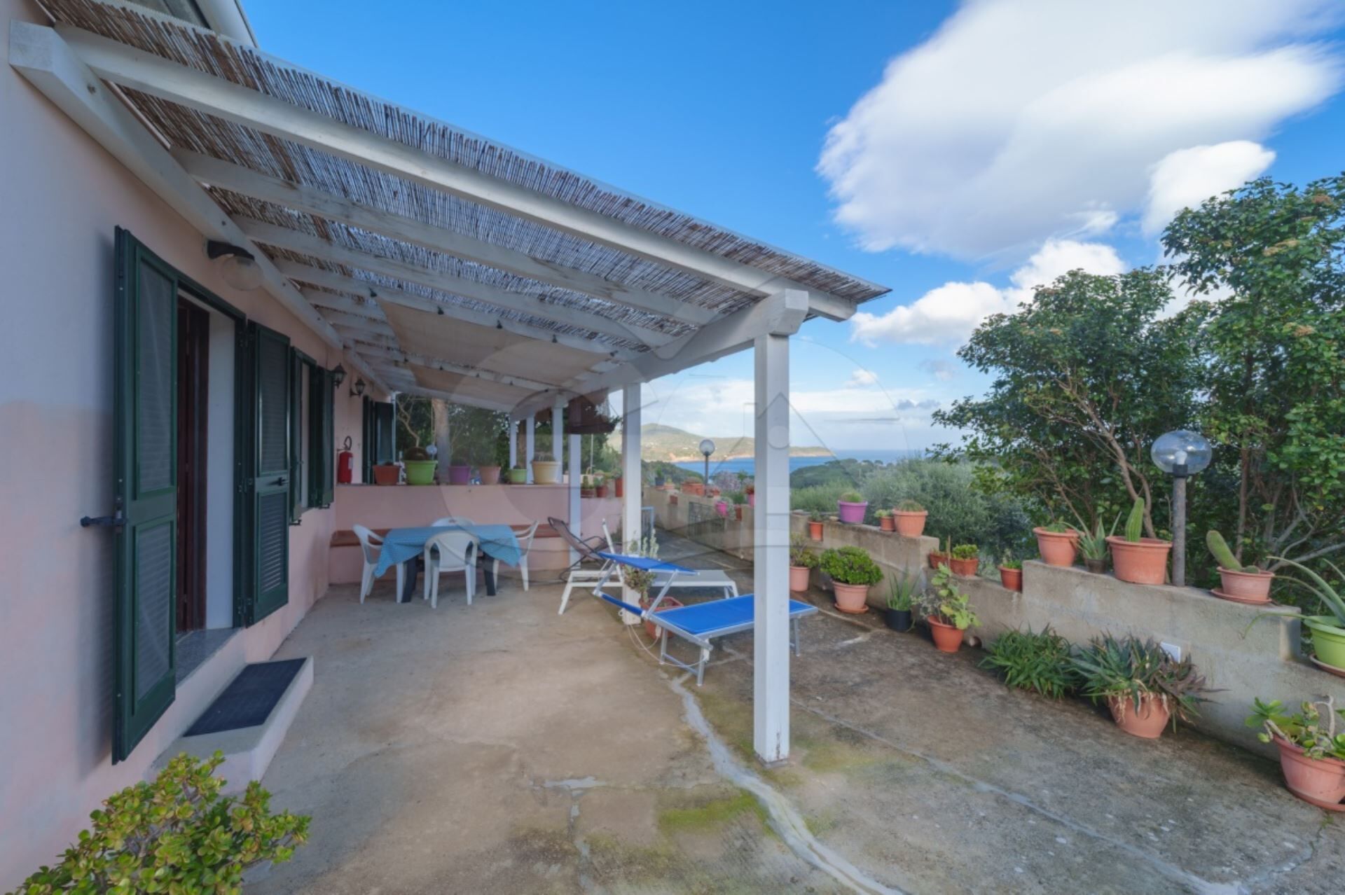 A covered patio area with a table and chairs, potted plants, and a view of the landscape.