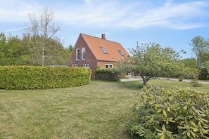 Une maison avec un toit en pente, une pelouse bien entretenue et un arbuste au premier plan.