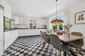 A modern kitchen with checkered flooring, white cabinets, and a dining area with chairs and a table.