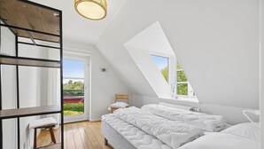 Um quarto com claraboia, uma cama, um banquinho de madeira e uma janela.