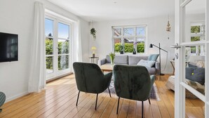 Uma sala de estar ampla com grandes janelas, uma televisão de tela plana e um espaço de estar aconchegante com sofá e poltronas.